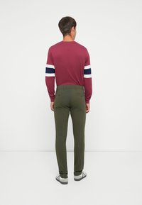 Burgundi hosszú ujjú póló, fehér és tengerészkék csíkokkal az ujján, olívazöld, slim-fit nadrággal párosítva. Kényelmes stílus, sima textúrával.