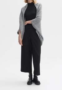 Szary teksturowany sweter rozpinany na przód, noszony na czarnym dopasowanym topie i luźnych czarnych spodniach; zestawiony z czarnymi masywnymi botkami za kostkę.