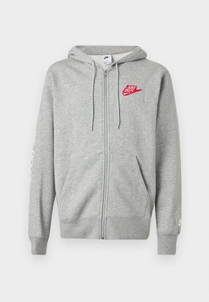 Ανοιχτό γκρι φούτερ με φερμουάρ, μπροστινές τσέπες, ρυθμιζόμενο κορδόνι στο κουκούλα και κόκκινο λογότυπο Nike "Just Do It" στο αριστερό στήθος.