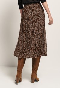 Jupe maxi en imprimé léopard en tissu léger et transparent ; présente une forme fluide avec un ourlet évasé, associée à des bottes marron en daim jusqu'aux genoux.
