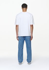 White cotton t-shirt with a relaxed fit and short sleeves, paired with blue denim jeans. The shoes are black and white sneakers.