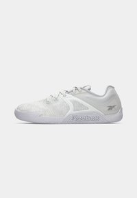 Baltas sporta apavi ar teksturētu tīkla augšdaļu, elastīgu gumijas zoli, mežģīņu dizainu un izteiksmīgu Reebok logo uz sāniem.