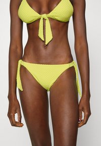 Conjunto de bikini verde limão com tecido texturizado, parte superior em triângulo com laço frontal e laterais ajustáveis nas calças.