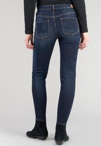 Vaqueros ajustados de color azul oscuro con un diseño ceñido, bolsillos traseros visibles y sutiles detalles de costura, combinados con botas negras de ante hasta el tobillo.