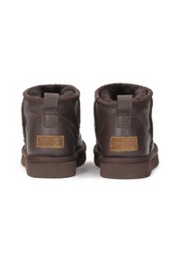 Botas de tobillo de cuero marrón con un acabado texturizado, forro interior suave y suela de goma plana. Presentan acentos de logo en la parte trasera.