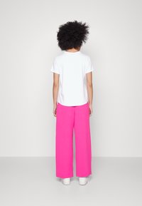 T-shirt blanc à manches courtes associé à un pantalon large rose vif. Le pantalon a une texture douce et une coupe décontractée. Porté avec des baskets blanches.