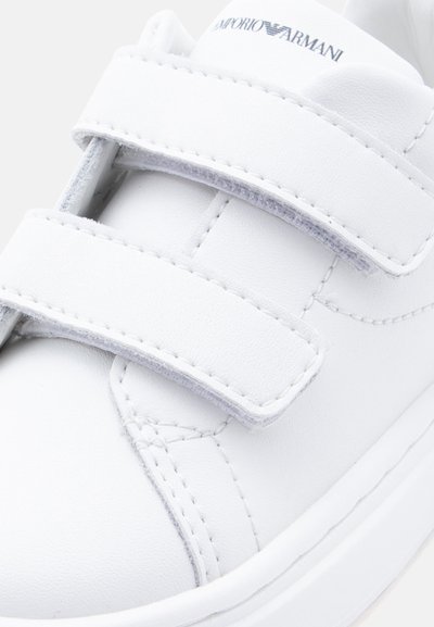 Λευκό αθλητικό παπούτσι Emporio Armani με δύο λουριά βέλκρο και ραφές διακόσμησης στο λείο δερμάτινο επάνω μέρος.