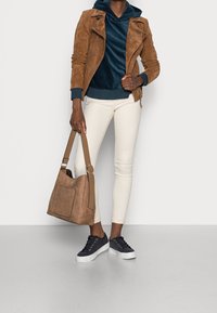 Tanfärgad mockajacka, marinblå sametshoodie, vita tajta jeans, brun axelväska, marinblå sneakers med vita sulor, guldöglor.