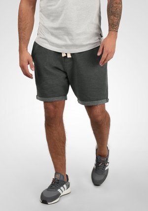 Grijze katoenen shorts met opgerolde zomen, voorzien van een crèmekleurige trekkoordsluiting. Gecombineerd met grijze sportschoenen en een lichtgrijs T-shirt.