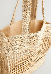 Flätad halm tote-väska i beige med vävt öppet mönster och två robusta tyghandtag; insidan har en enkel beige foder.