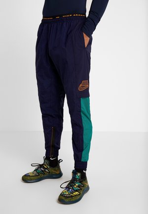 Granatowe i turkusowe dresy sportowe z elastycznym pasem, bocznymi kieszeniami i pomarańczowym logo Nike. W zestawie z kolorowymi, wzorzystymi sneakersami.