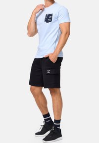 T-shirt azzurro chiaro a maniche corte con una tasca sul petto a motivo blu navy, abbinata a pantaloni cargo neri con tasca laterale e ricamo. Sneakers nere.