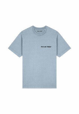 Jeune homme et femme portant des t-shirts décontractés « You & Me Tonight » dans un parc avec des fleurs, des bâtiments historiques et une grande roue en arrière-plan.