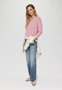 Lichtroze ribbed lange mouwen top, gecombineerd met vervaagde blauwe straight-leg jeans. Beige jasje om de taille geknoopt en crèmekleurige puntige hakken.
