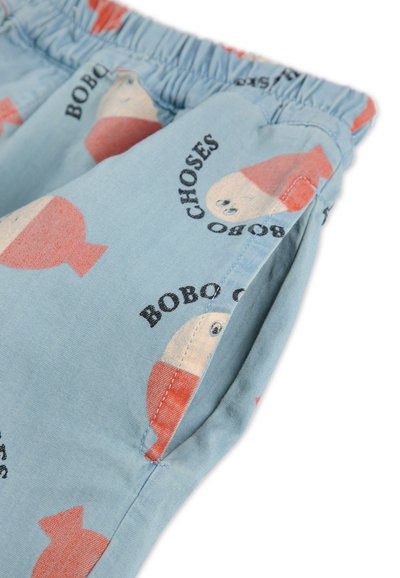 Pantalones cortos de tela azul claro con patrones de muñecos en rojo y beige, y texto negro "BOBO CHOSES". Cintura elástica con bolsillos laterales.