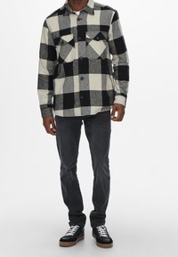 Czarna i biała, w kratkę flanelowa koszula z dwiema kieszeniami na piersi, długimi rękawami, z guzikiem z przodu i kołnierzykiem. Połączona z ciemnymi dżinsami i czarnymi tenisówkami.