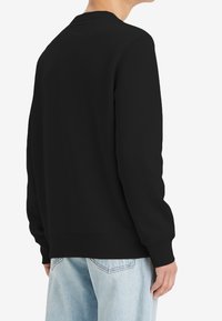 Zwarte trui met een ronde hals en lange mouwen, gemaakt van gladde stof. Voorzien van geribbelde manchetten en zoom, met een losse pasvorm.