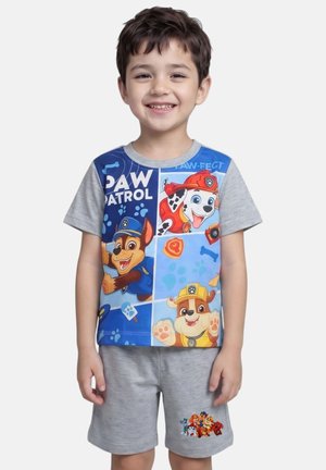 Garçon souriant portant un t-shirt gris Paw Patrol avec les personnages Chase, Marshall et Rubble et un short gris assorti avec imprimé Paw Patrol.