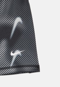 Közelkép fekete és szürke csíkos anyagról, fehér Nike pipa logóval és a szegélyen látható varrással.