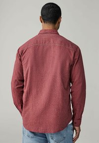 Chemise à manches longues rouge à motifs avec un col classique, des poignets à boutons et un design géométrique subtil, fabriquée en tissu doux et offrant une coupe décontractée.