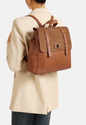 Zaino in pelle marrone con patta in suede, dotato di doppie cinghie, hardware in metallo e finitura texturizzata, esposto su uno sfondo neutro.