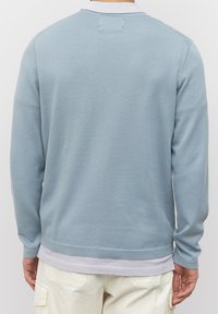 Maglione azzurro chiaro a girocollo, texture lavorata a maglia, maniche lunghe, orlo e polsini a coste, indossato sopra una camicia bianca, tessuto morbido.