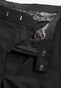 Čierne nohavice so zipsom, gombíkom a háčikovým zapínaním, s podšívkou z vzorovanej látky s paisley vzorom vo vnútri pásu.