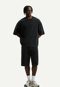 Černé oversized tričko a kraťasy ke kolenům s vybledlou džínovou texturou. Kombinováno se světlými teniskami a bílými ponožkami.