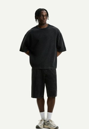 Černé oversized tričko a kraťasy ke kolenům s vybledlou džínovou texturou. Kombinováno se světlými teniskami a bílými ponožkami.