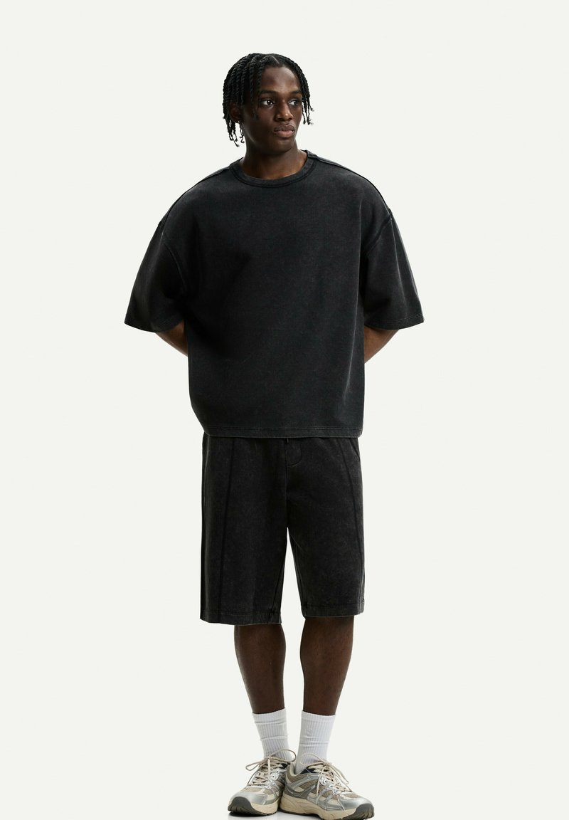 Černé oversized tričko a kraťasy ke kolenům s vybledlou džínovou texturou. Kombinováno se světlými teniskami a bílými ponožkami.