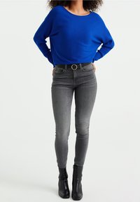 Sininen ribbattu neule, rento istuvuus, pyöreä pääntie. Harmaat slim fit -farkut, korkea vyötärö, vyö, jossa on pyöreä solki. Mustat nilkkurit.