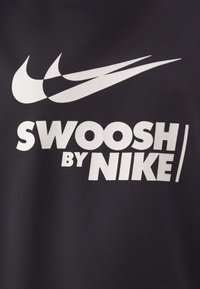 T-shirt di stoffa nera con grande testo e logo bianco "Swoosh by Nike", texture liscia e design grafico audace.