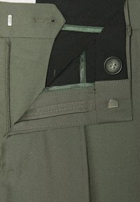 Grønne bukser med et glat stof, der har en lynlåsgylp, metalknap og broderede detaljer. Den indvendige talje har en kontrasterende tekstur.