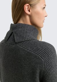 Pull en tricot gris avec un col montant côtelé et un corps texturé. Tissu lisse avec un éclat subtil, mettant en valeur un design unique au dos.