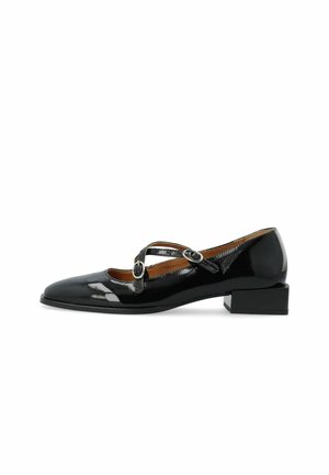Black patent leather low-heeled shoe with a pointed toe, featuring crossed straps with circular hardware details for secure fastening.