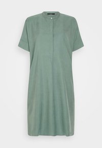 Zelené šaty s krátkým rukávem a kulatým výstřihem, které mají malé zapínání na knoflík vpředu a volný, splývavý střih.