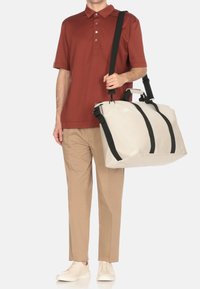 Tan trousers, red collared shirt, and white slip-on shoes. Gray bag with black straps. Features rectangular shape and sturdy handles.