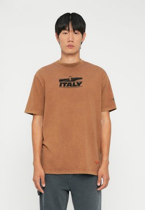 Barna pamut póló kerek nyakkivágással, fekete nyomott "ITALY" felirattal és egy kis piros logódísszel az alján. Rövid ujjú.