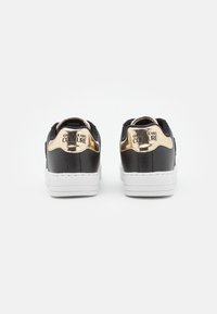 Svarta och gyllene sneakers med en slät läderöverdel, vit sula och subtil branding på hälen; har en minimalistisk design.