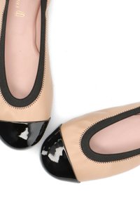 Ballerines en cuir beige avec bouts en cuir verni noir; bords élastiqués avec couture contrastante noire; texture lisse avec forme arrondie.