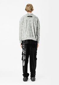 Suéter gris texturizado con cuello redondo, combinado con pantalones cargo negros que cuentan con bolsillos de utilidad y detalles impresos, llevados con zapatos negros gruesos.