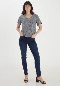 Top a V a righe in bianco e nero con maniche corte a volant, abbinato a jeans aderenti blu scuro e sandali neri con tacco a blocco.