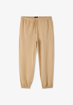 Beżowe spodnie dresowe wykonane z miękkiego materiału, z elastycznym pasem i sznurkiem do regulacji. Mankiety na nogawkach zapewniają zwężany krój.