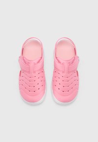 Rausvos spalvos vaikų klumpės su patraukliu paviršiumi, atvira kulne ir reguliuojama diržele, su išpjautomis skylutėmis vėdinimui ir baltu padu.