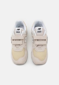 Une paire de baskets New Balance 574 beige et crème avec un tissu en maille et de doubles bandes Velcro, vue d'en haut sur fond blanc.