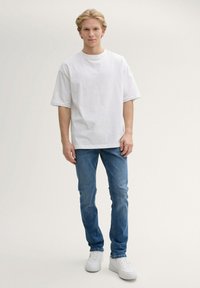 Camiseta de algodón blanca y holgada con mangas cortas, combinada con jeans de mezclilla azules y zapatillas blancas. Diseño sencillo, ajuste relajado.