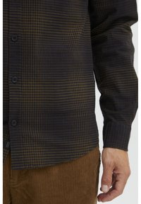 Dark plaid shirt featuring blue and brown tones, made of textured fabric, with a button-down front and long sleeves.