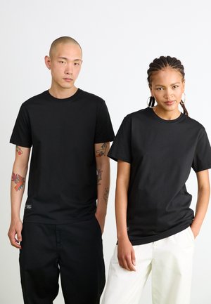 T-shirts en coton noir avec un design classique à col rond, portés par deux personnes. Présentent une texture douce et une coupe décontractée.