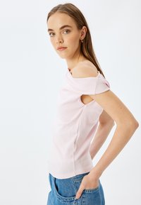 Rosa avskuren topp med korta ärmar, texturerat bomullsmaterial, figurnära design och detalj med rundad halsringning. I kombination med högmidjade jeans.