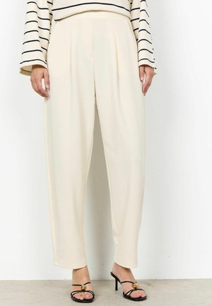 Persona che indossa pantaloni larghi color crema, sandali neri con tacco alto e cinturini, e una maglia a maniche lunghe color crema con righe orizzontali nere.